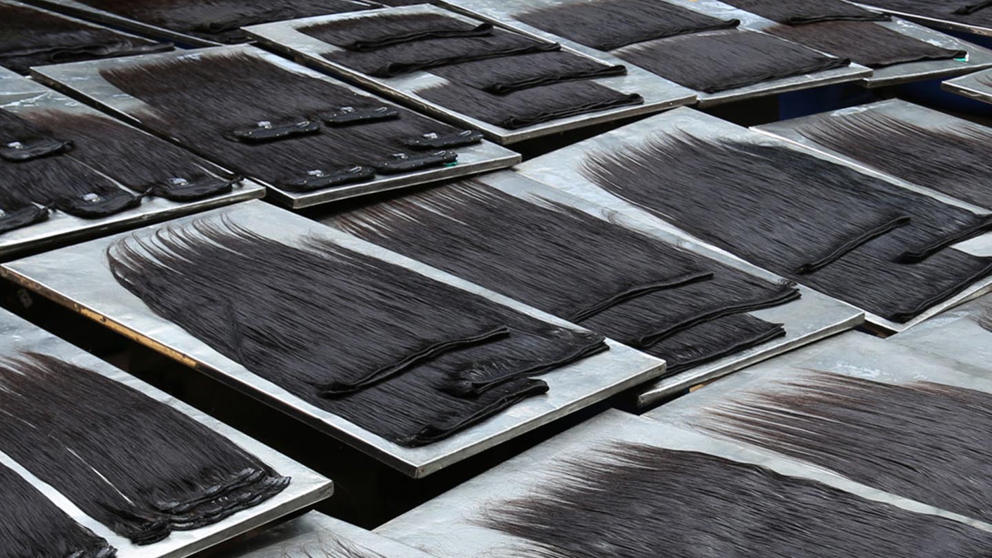 Trays with long, dark Asian hair extensions or wigs neatly spread out and arranged in rows, likely drying or being prepared for processing in a factory setting.