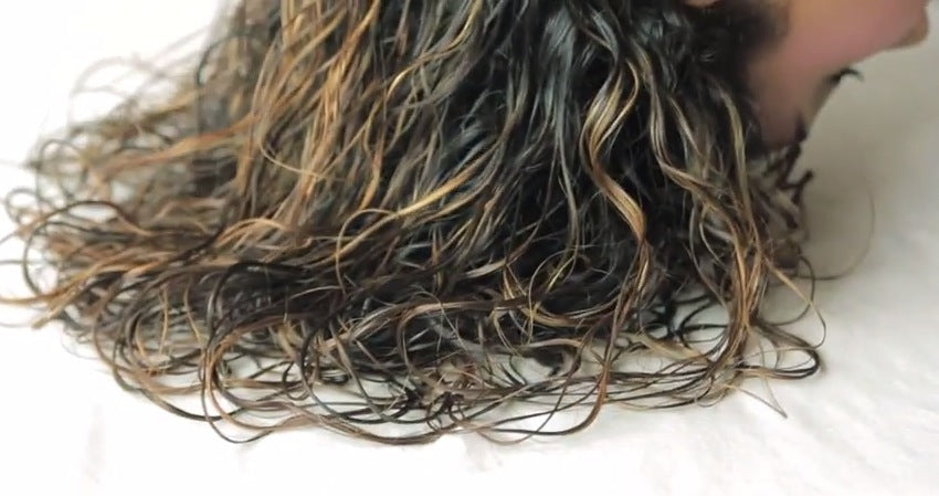 A close-up of wet, curly hair with light brown and blonde highlights, spread out over a white surface.