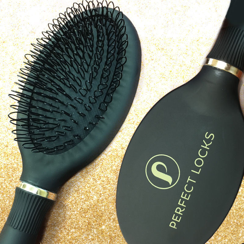 Two black hairbrushes with gold accents are displayed on a glittery gold surface. One reveals its bristles, while the other shows the Perfect Locks logo.