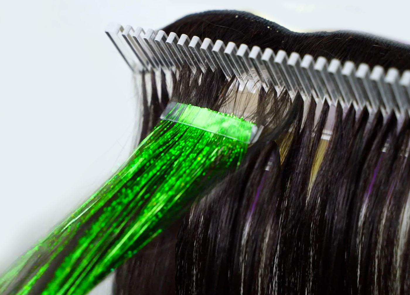 A close-up of a hair extension tool attaching a bright green, shiny strand using Hair Tinsel Methods to dark natural hair.