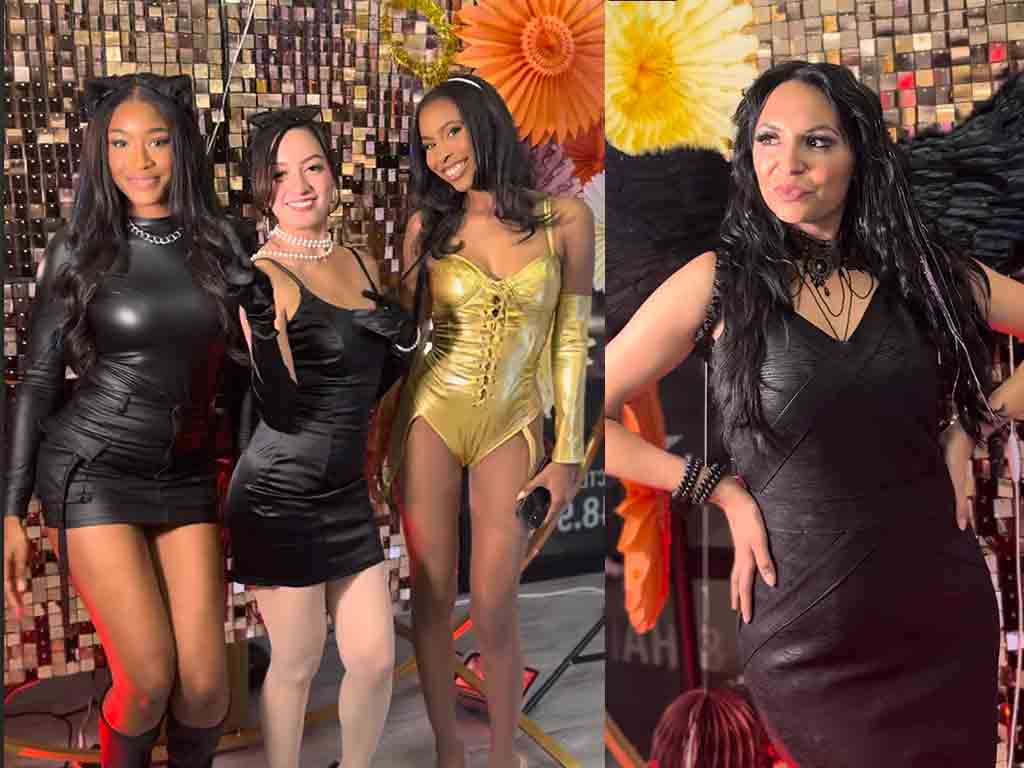 Four women pose at a glam Halloween Bash; three stand together in black and gold dresses before a shiny backdrop, while one stands separately in a black dress, making a playful face.