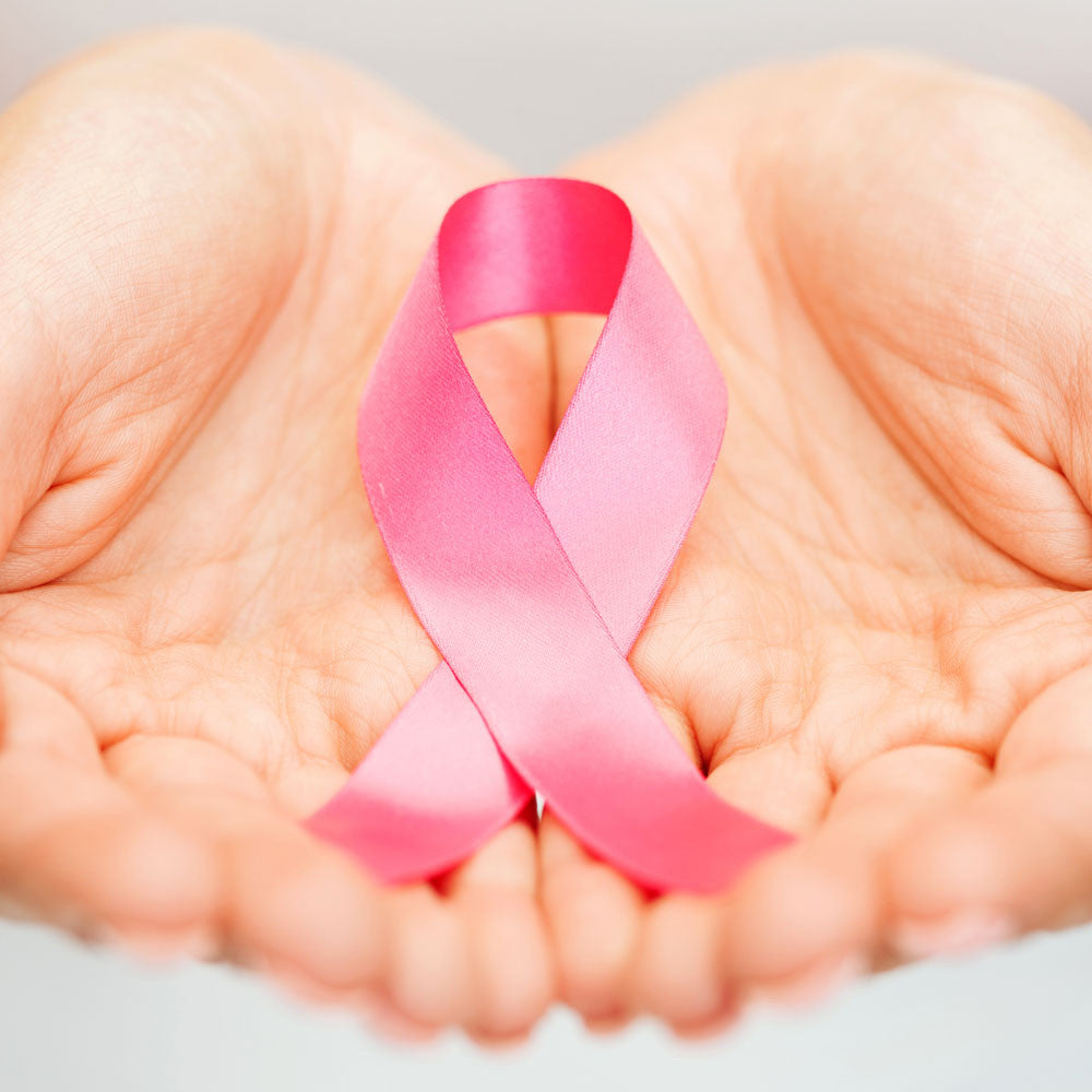 A pair of cupped hands holds a pink ribbon, symbolizing breast cancer awareness and PINKTOBER, against a soft, light background, highlighting hope and hair options for cancer survivors.