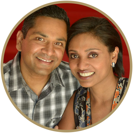 A smiling couple poses closely together in front of a red background.