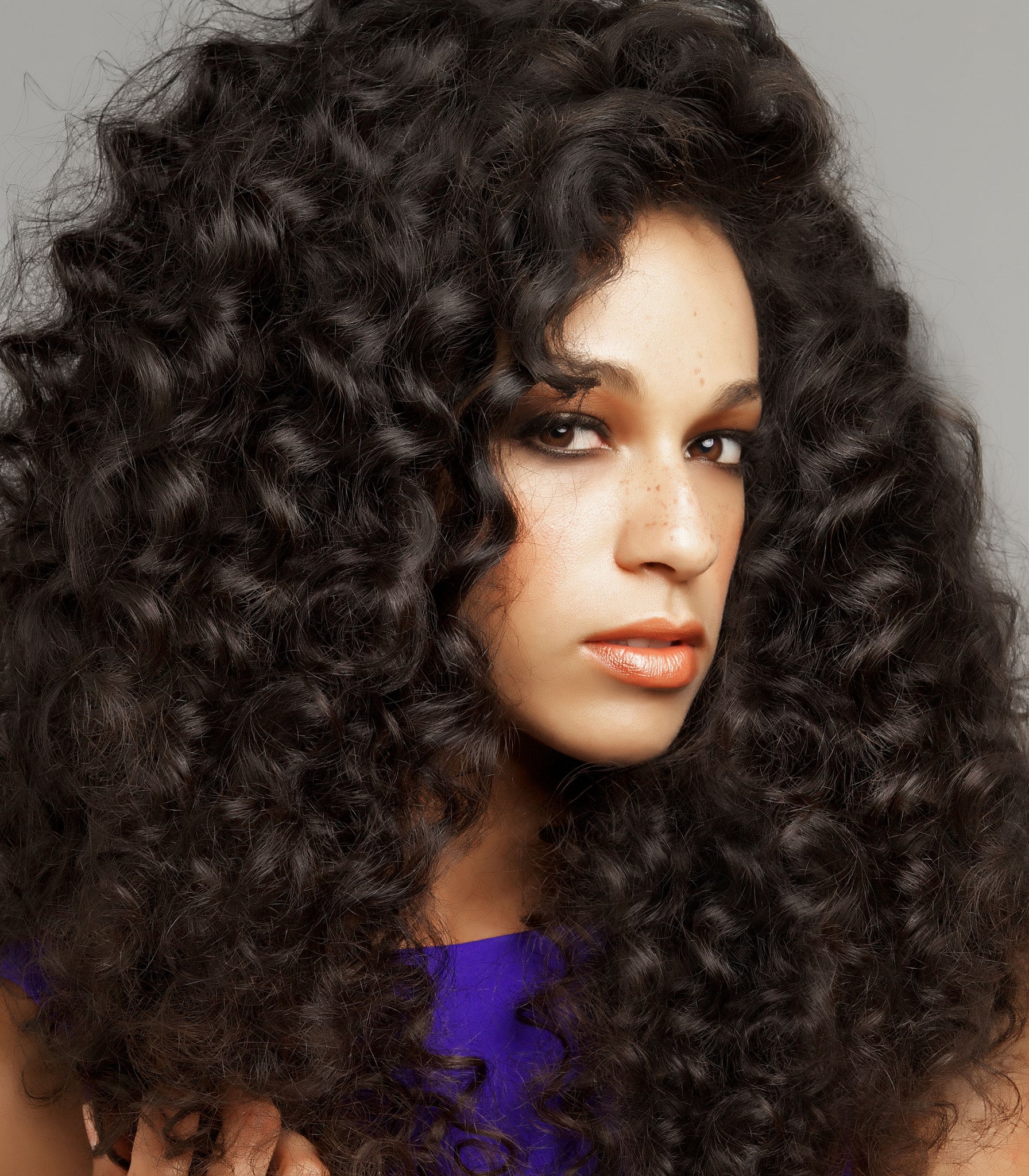 A woman with voluminous, curly virgin Indian hair and light makeup gazes toward the camera.