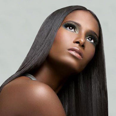 A woman with long, straight, dark hair gazes upward, showcasing flawless skin, dramatic eye makeup with bold lashes, and glossy lips, an image that invites you to spoil your locks with luxurious hair care.