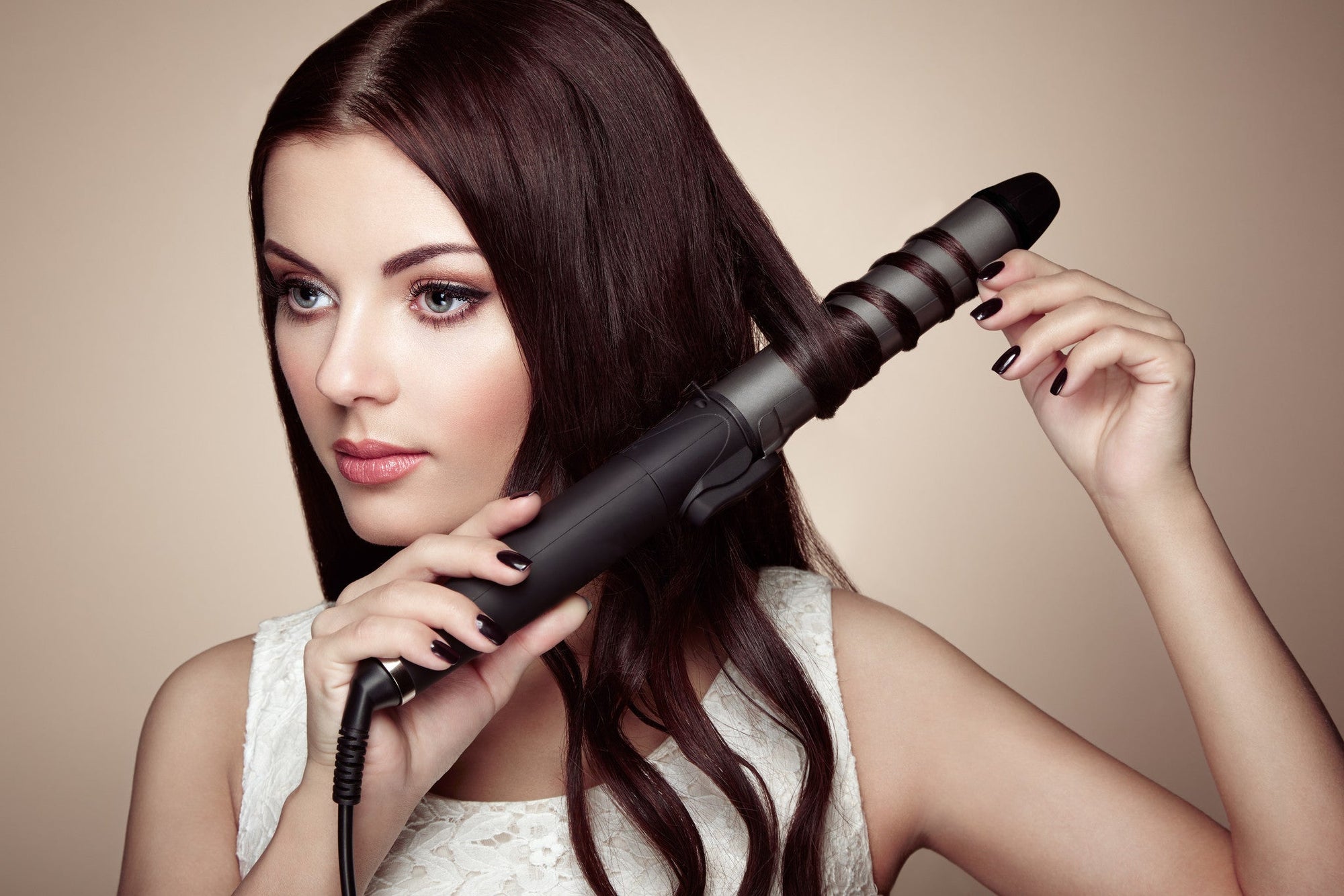 A woman with long brown hair uses a curling iron to style her perfect locks.