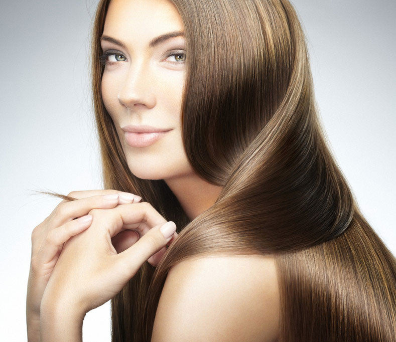A woman with smooth, shiny, straight brown hair poses with her hands near her face, looking at the camera.
