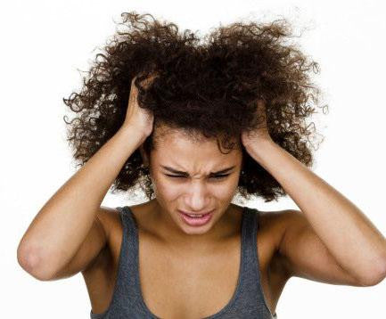A person with curly hair wearing a sleeveless top is holding their head with both hands, looking frustrated or stressed, possibly trying to relieve an itchy scalp from a sew in weave.