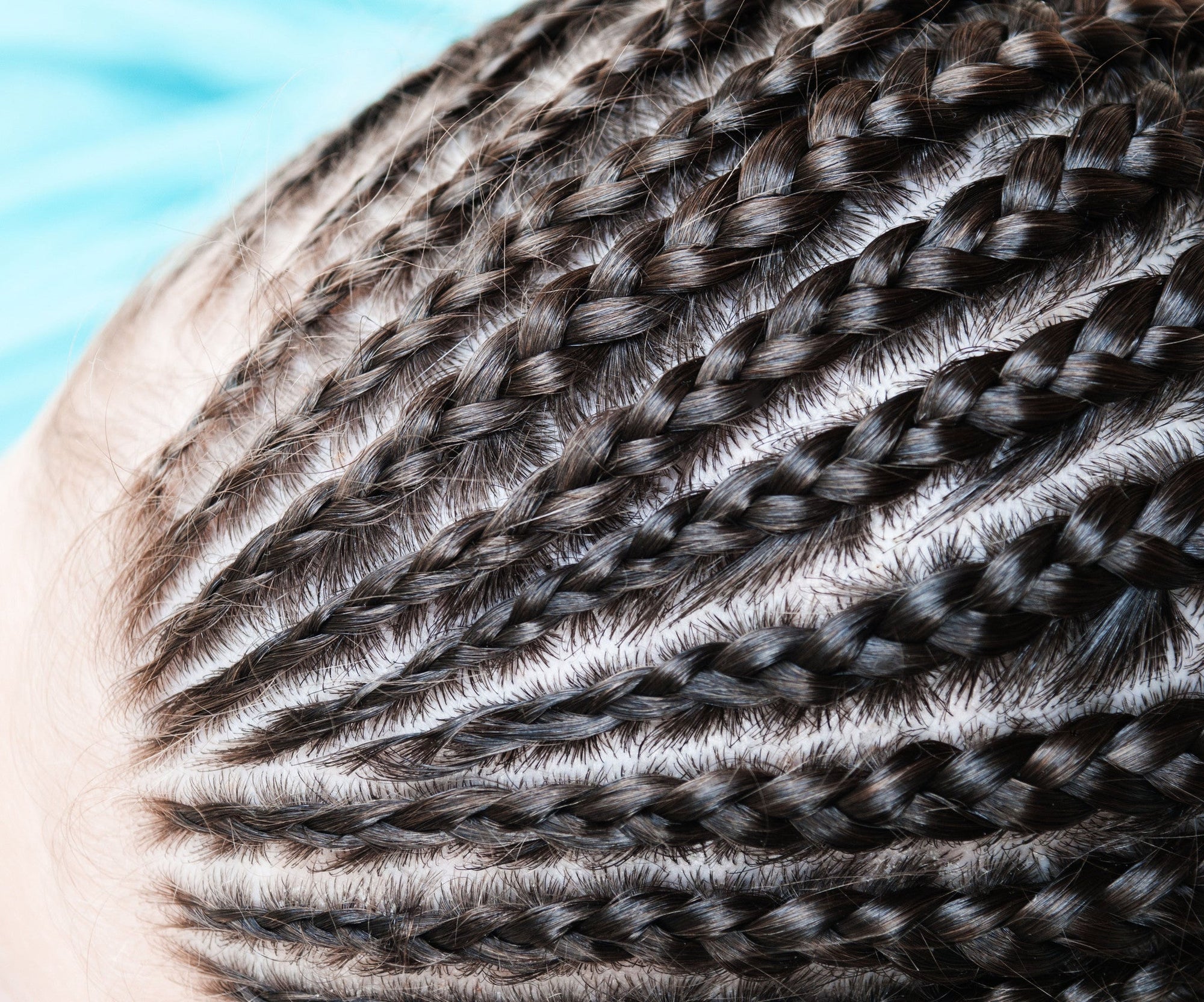 Close-up of a person's scalp with neatly styled cornrow braids, showing intricate, parallel rows of dark hair tightly woven against the scalp.