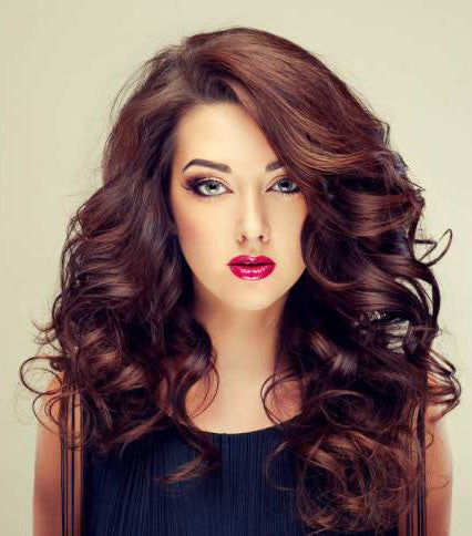 A woman with long, voluminous Type 2 wavy hair and bold makeup featuring red lipstick gazes directly at the camera.