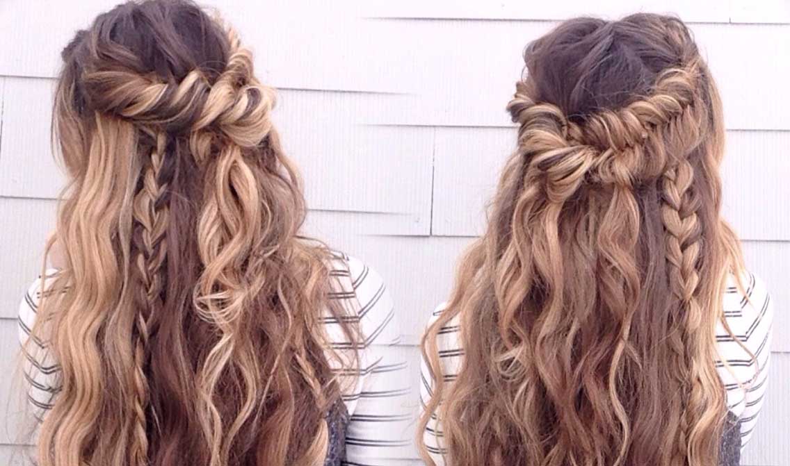 A person with long, wavy brown and blonde hair styled in a half-up, braided hairstyle with twisted sections showcases a chic Boho Braids look, standing against a light-colored wall.