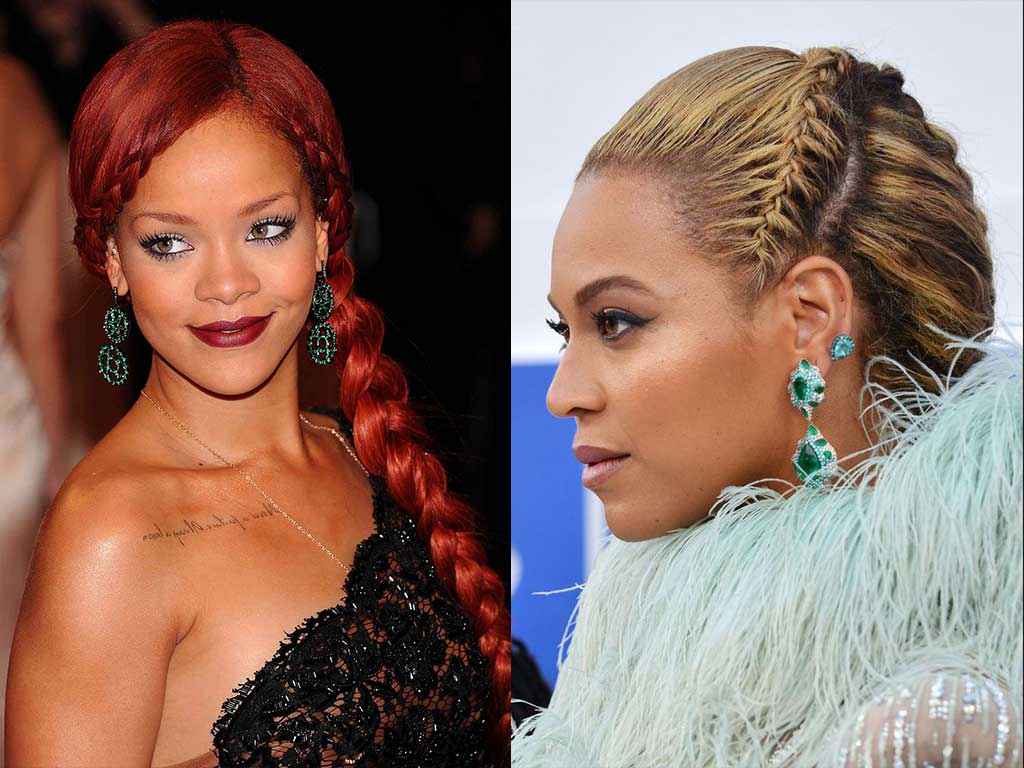 Two women facing opposite directions, both wearing elaborate French braid hairstyles, statement earrings, and glamorous outfits, one with long red hair and the other with blonde hair styled in a side braid.