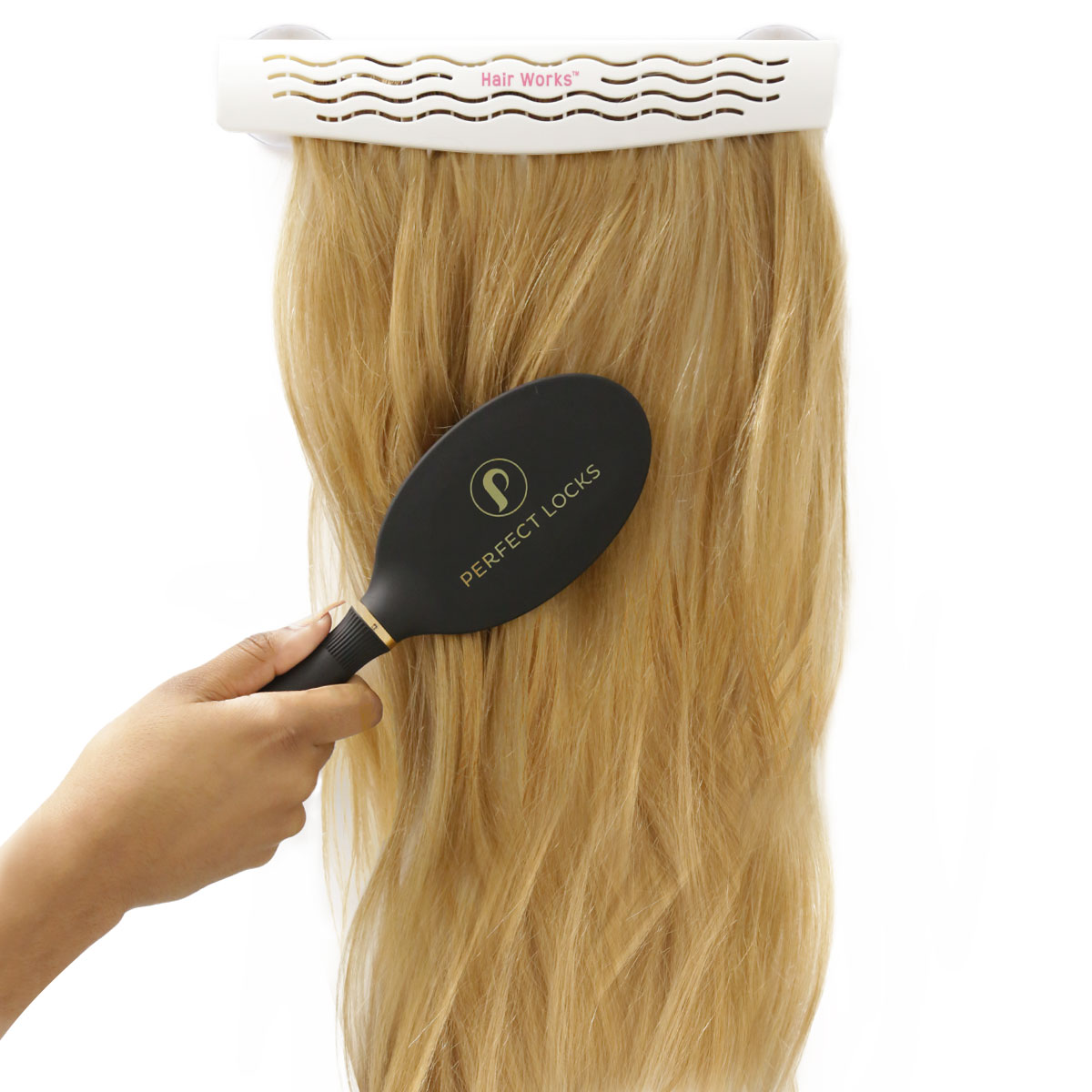 A hand uses a black brush labeled Perfect Locks to brush long, blonde hair extensions hanging from a white Hair Works holder, demonstrating proper hair extensions care.