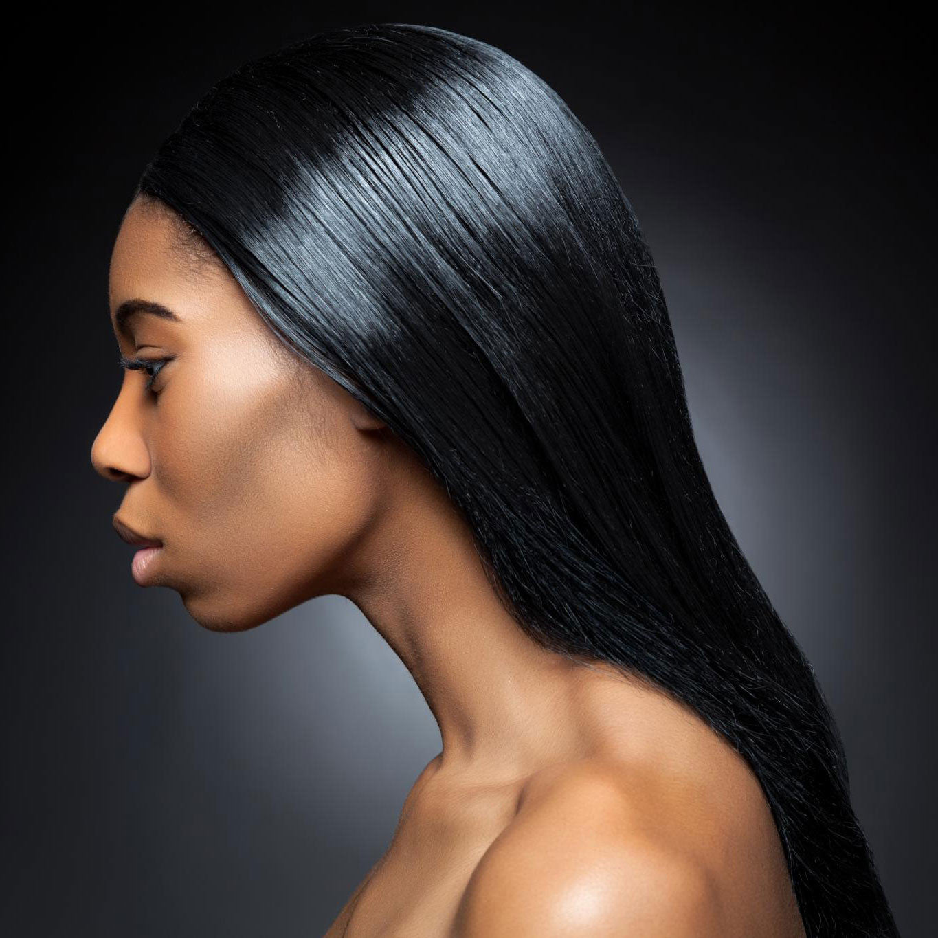 Profile view of a woman with smooth, straight, shiny black hair and glowing skin, set against a dark gradient background.