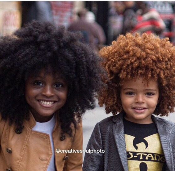 Two smiling children with big, curly African American hair stand side by side.