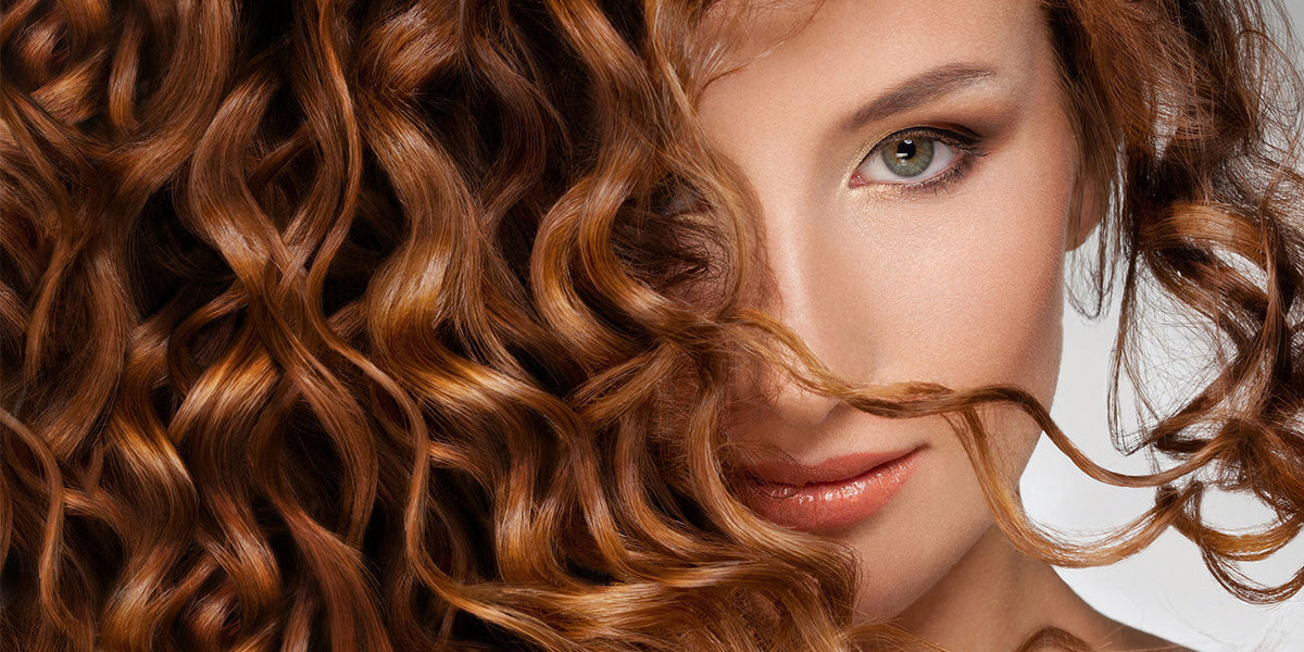 Woman with long, shiny reddish-brown curls styled with Perfect Locks brown tape-in extensions