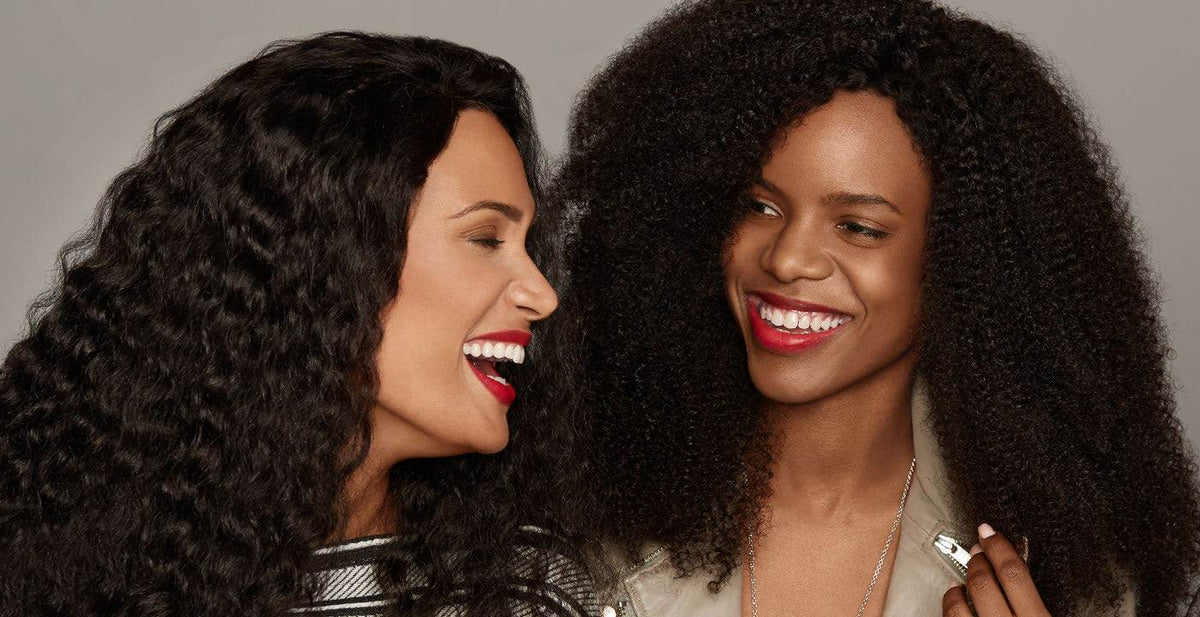 Two happy women wearing Perfect Locks curly lace front wigs with red lipstick and stunning curls