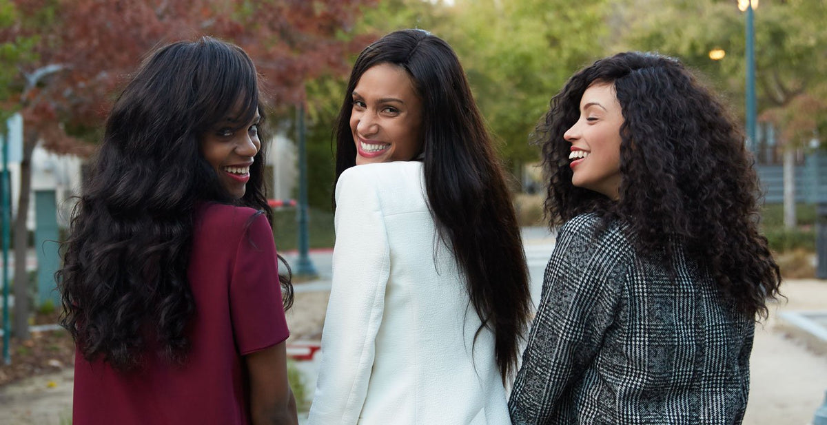 Three women with long, dark Perfect Locks virgin hand-tied wefts smiling outdoors in a lush setting