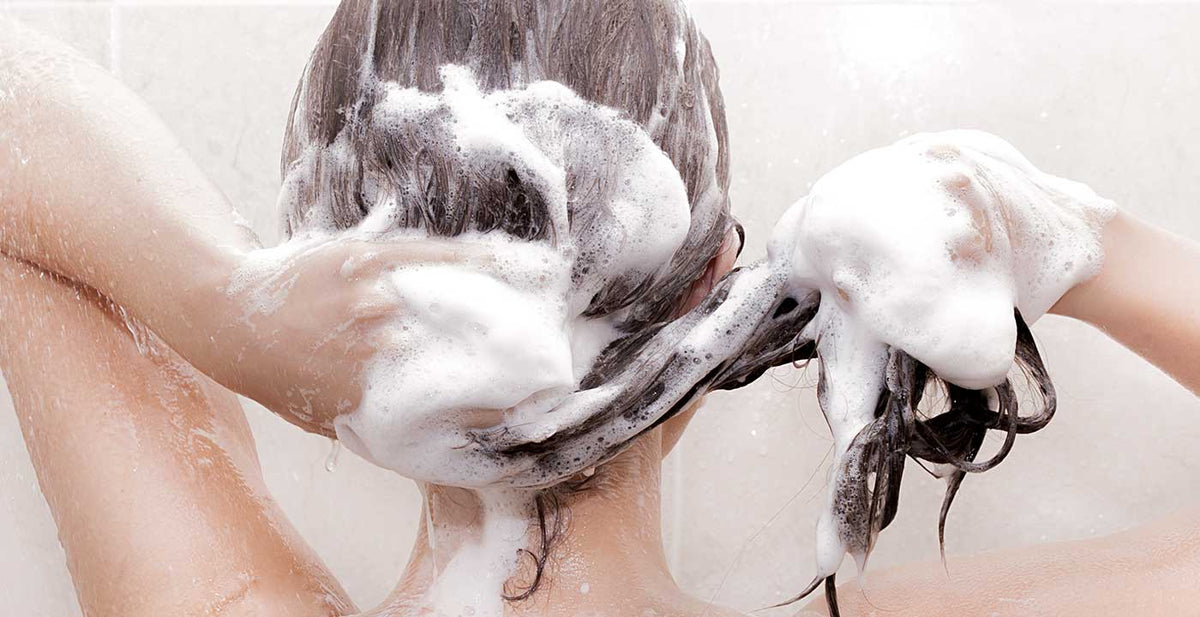 Person using Perfect Locks hair care for extensions, lathering sulfate-free shampoo in the shower
