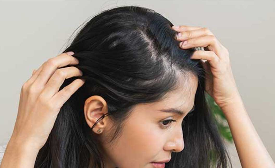 Woman parting her hair to examine roots, considering Perfect Locks extensions for hair loss