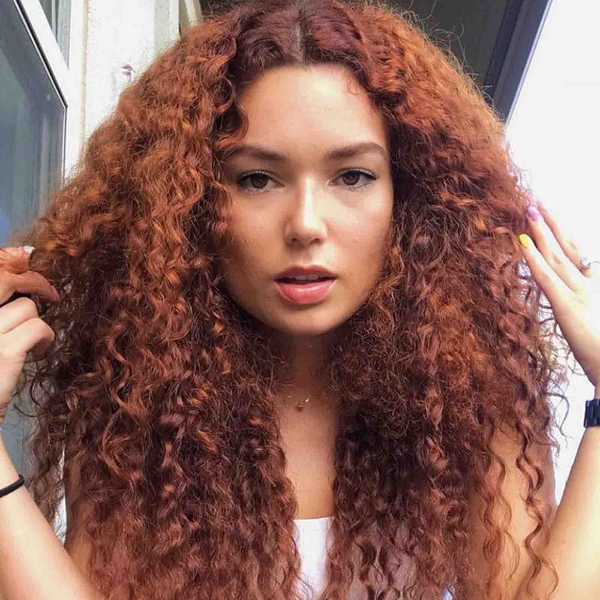 Woman with long, voluminous dark auburn curly hair extensions posing outdoors, showing defined curls and natural texture.
