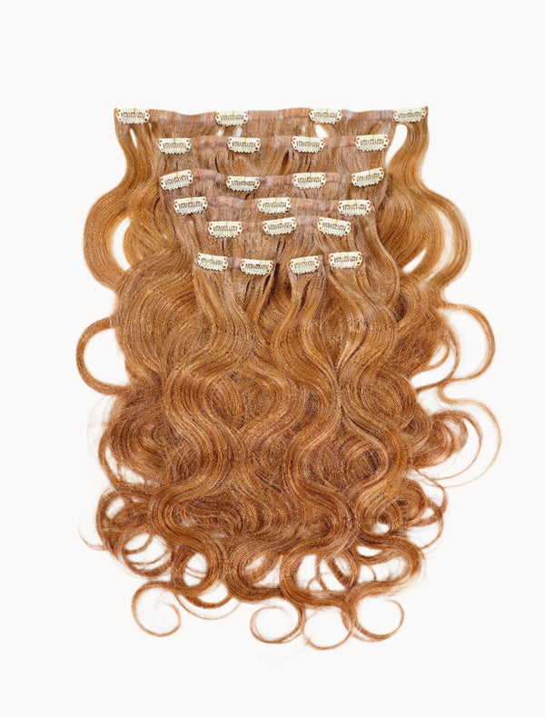 Wavy, reddish-brown clip-in hair extensions with subtle highlights on a white background, showing multiple wefts with metal clips.