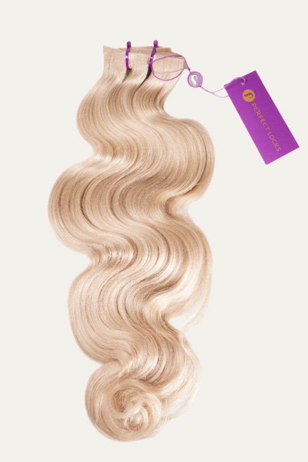A bundle of wavy, blonde hair extensions secured with two purple bands and a Perfect Locks tag on a plain white background.