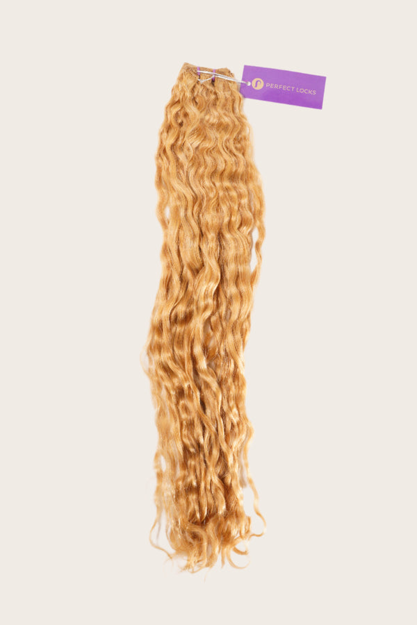 A bundle of long, wavy, honey-blonde hair extensions with a purple Perfect Locks tag on top against a plain light background.