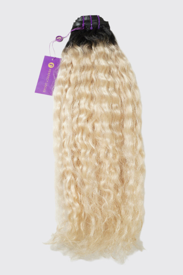 A bundle of ombre wavy hair extensions, dark roots fading to light blonde ends, secured with a black and purple band and purple tag.