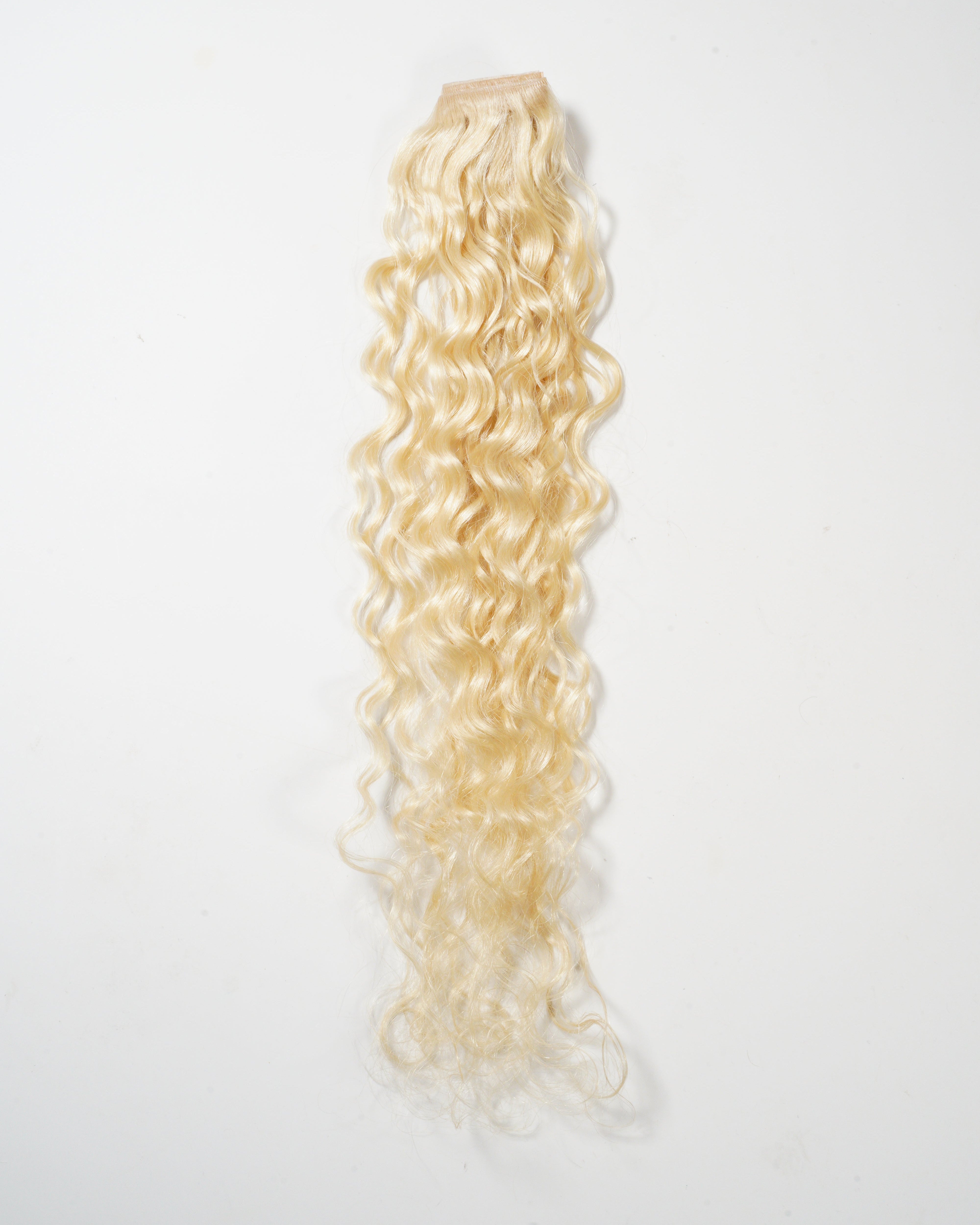 A long, blonde, curly hair extension with a sewn weft at the top is displayed on a white background, showcasing its voluminous texture.