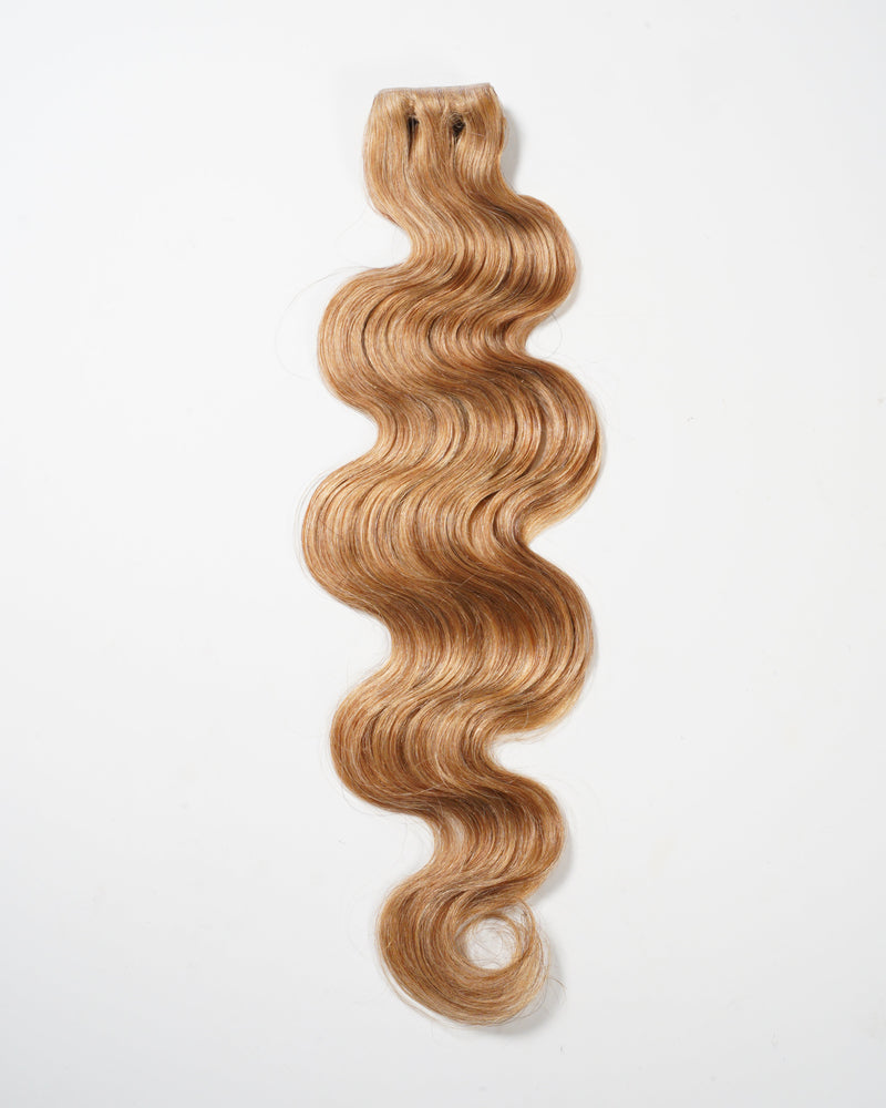 A single piece of long, wavy, light brown hair extension is displayed flat against a plain white background.