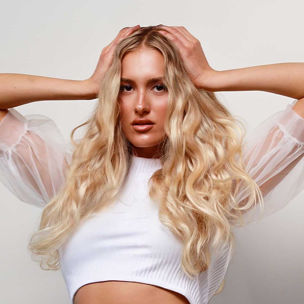 Woman with long blonde hair wearing a white top against a light background