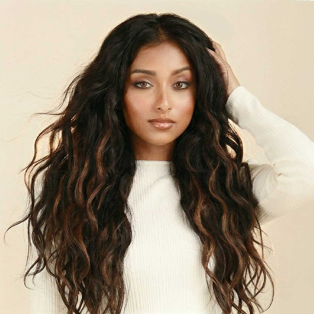 Woman with long voluminous dark wavy hair extensions touching her hair, wearing a white top against a warm cream background, showcasing Perfect Locks Remy human hair extensions