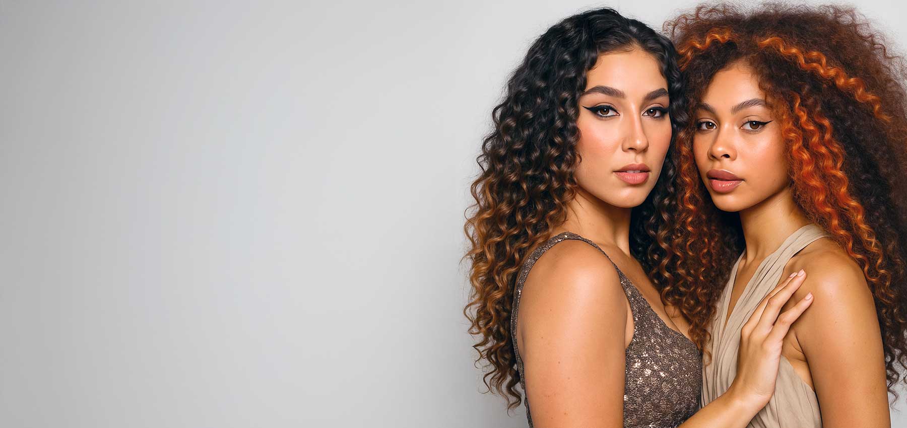 Two women with curly hair standing close together against a plain background