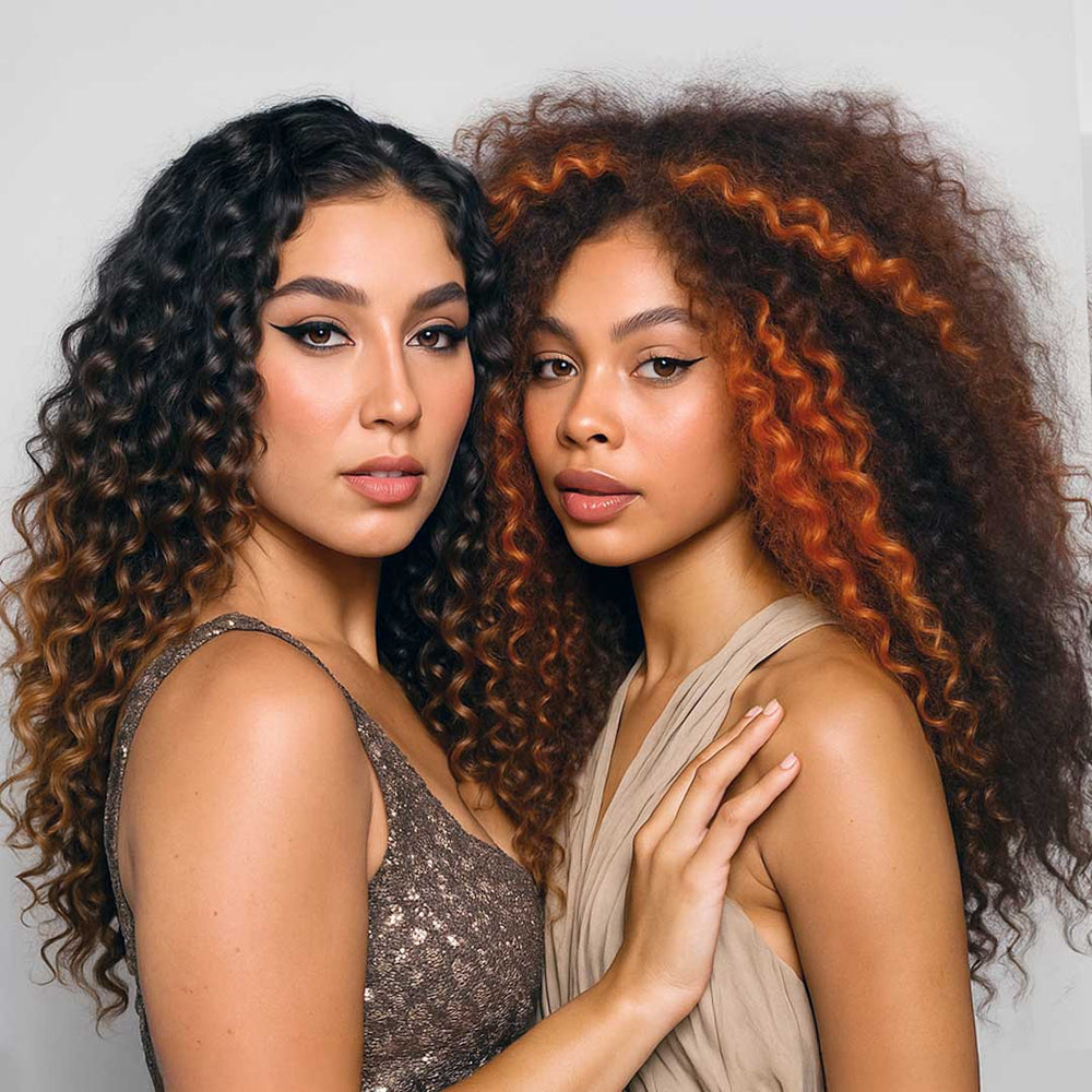 Two women with beautiful curly hair extensions posing against a plain background