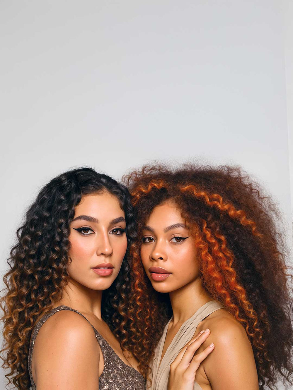 Two women with curly hair posing against a plain background