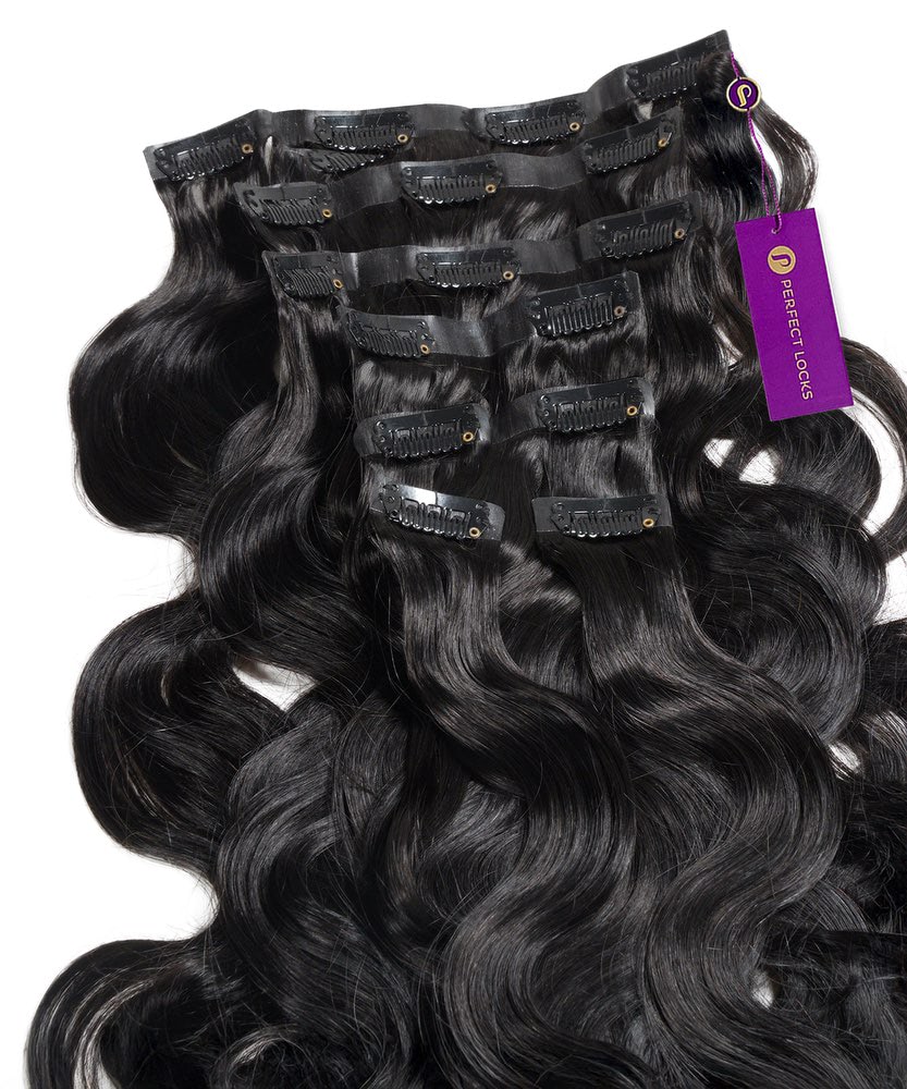 Several jet black, wavy Seamless Clip-In Hair Extensions from Perfect Locks are arranged side by side. A purple Perfect Locks tag is attached to one of the premium human hair extensions.#color_jet-black-(1)