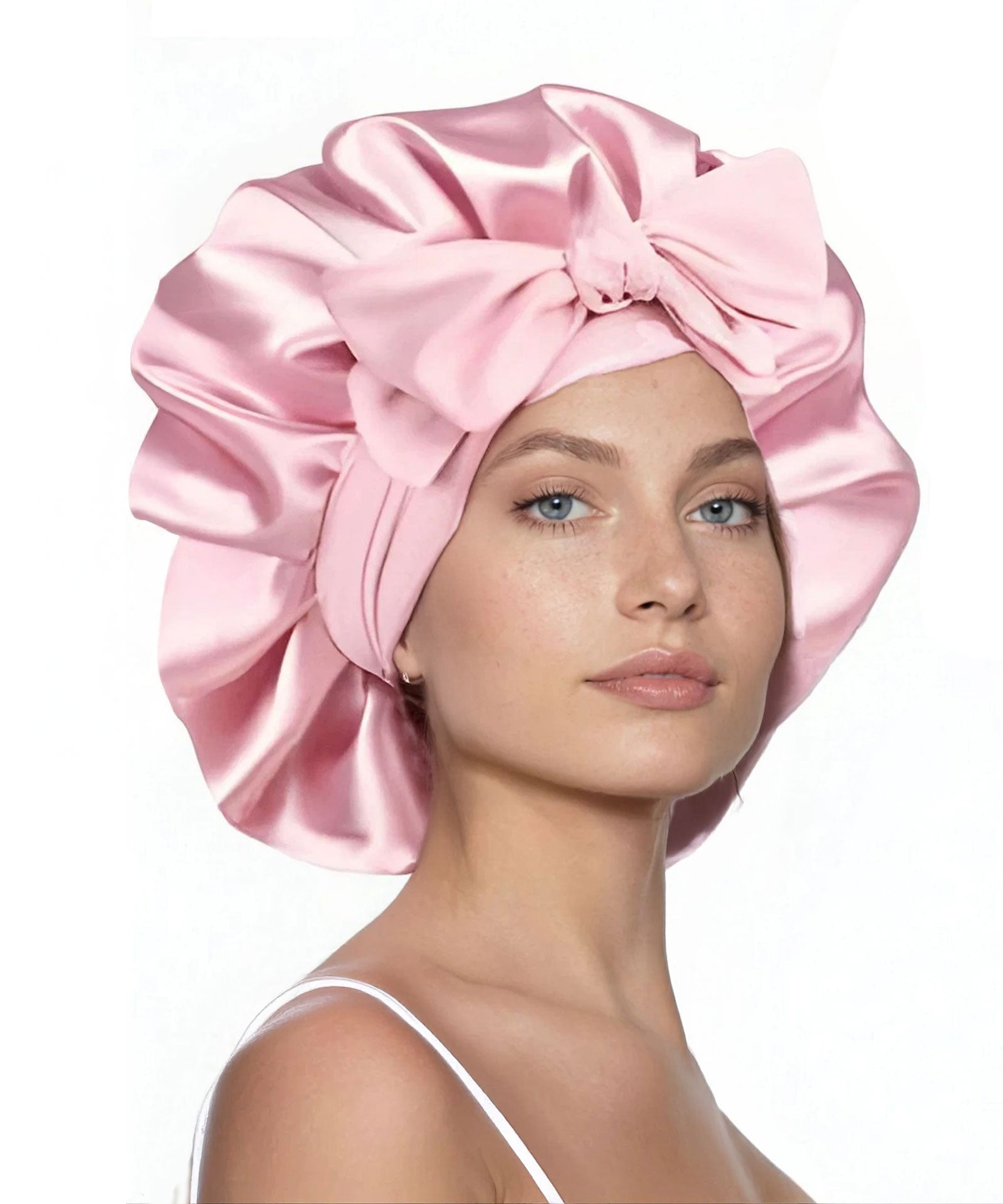 A woman wears a large, shiny pink satin bonnet with a big bow on the front, confidently gazing at the camera against a white background.