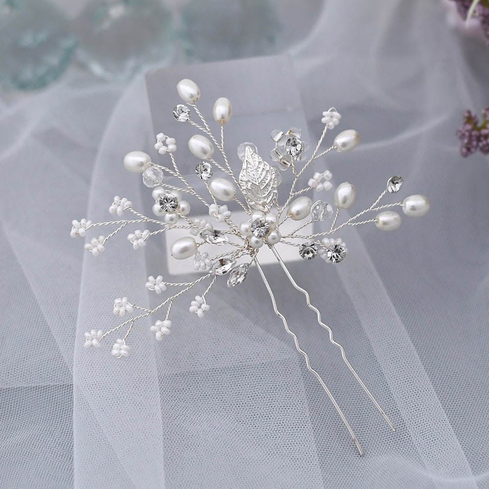 A decorative silver hairpin with delicate wire branches, faux pearls, crystals, and small silver leaves rests on sheer white fabric.