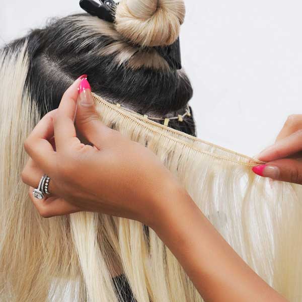Stylist installing blonde hand-tied weft extensions onto a client’s natural hair using beaded row technique.
