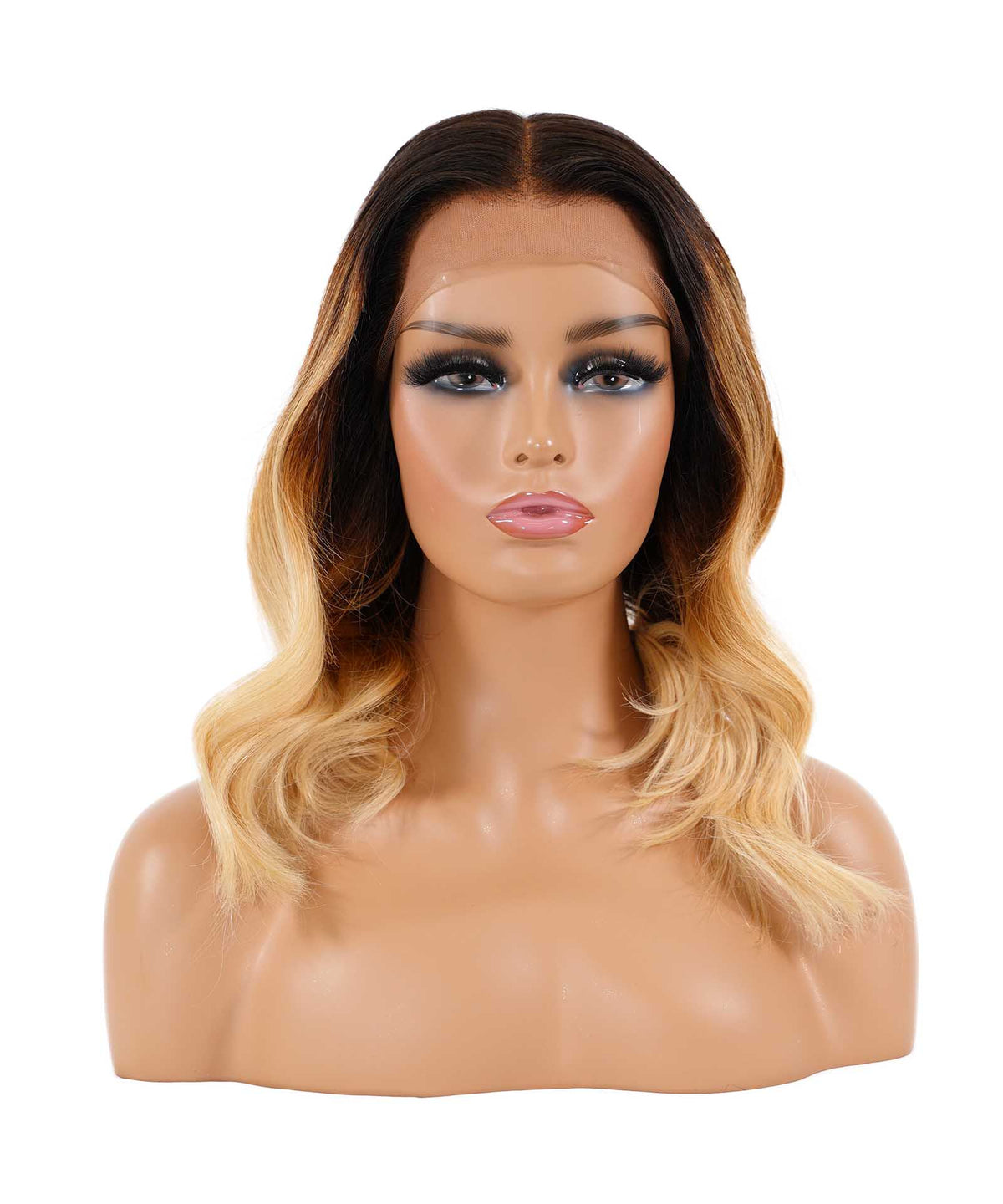A mannequin head displays a shoulder-length wig with dark roots and blonde ombre waves, styled in soft curls. The mannequin features defined eyebrows, dramatic eye makeup, and pink lips.
