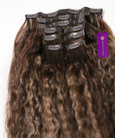 A set of Curly Seamless Clip-In Hair Extensions in rooted ash blonde highlights, with clip attachments and a purple Perfect Locks tag.#color_rooted-ash-blonde-highlights-(4/26/4)