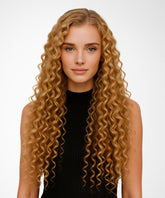 A woman wears the Perfect Locks Curly U-Part Wig in Honey Blonde and a sleeveless black top, looking at the camera against a plain white background.#color_honey-blonde-(27)