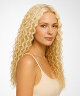 A woman with light skin wears a Platinum Blonde Curly U-Part Wig by Perfect Locks and a beige tank top, standing against a plain white background and looking at the camera with a neutral expression.#color_platinum-blonde-(613)