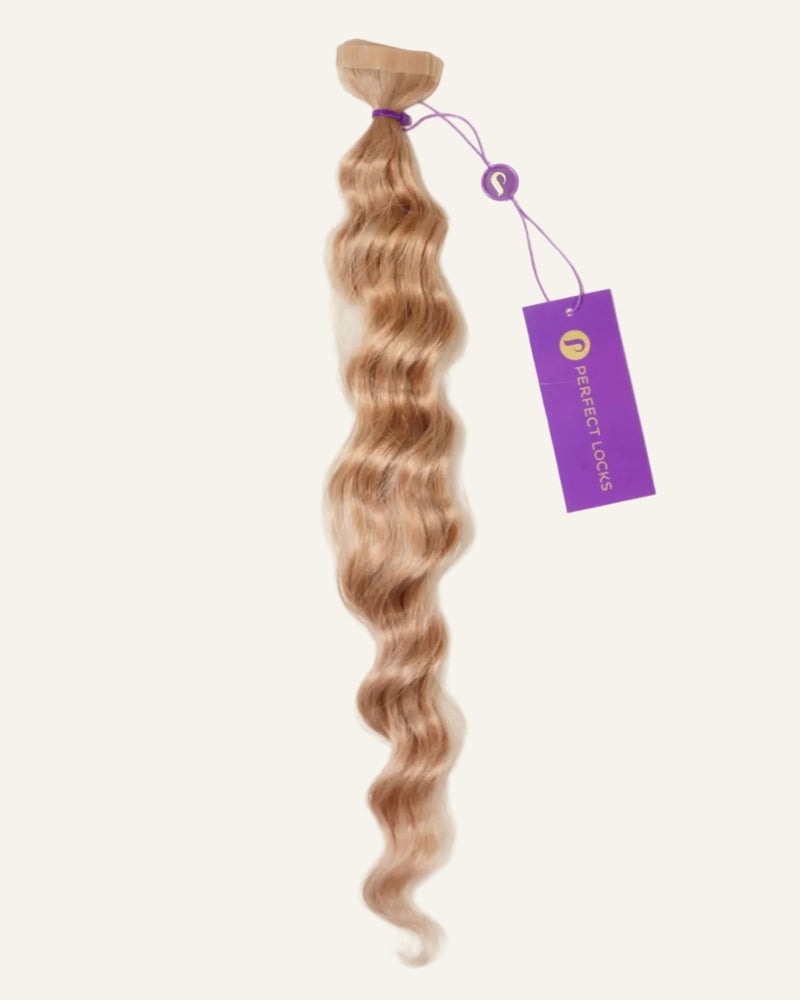 A bundle of long, wavy, light brown hair extensions is secured with a purple band and features a purple Perfect Locks tag, displayed against a plain, light background.