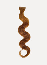 A long, wavy strand of reddish-brown hair extension with a neat, curled tip rests elegantly against a white background.