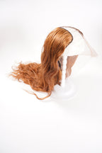 A long, wavy auburn lace front wig is styled on a white mannequin stand against a plain background.