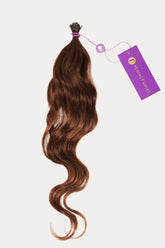 A bundle of wavy, brown hair extensions is tied at the top with a purple string and has a tag labeled Perfect Locks for luxury.