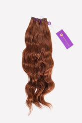 A bundle of long, wavy, reddish-brown hair extensions tied at the top with a purple tag. Displayed on a white background.