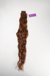 A long, wavy bundle of reddish-brown hair extensions secured at the top with a purple band and tag, on a white background.